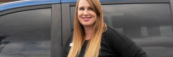Car-Mart Associate Mandy Owens smiles posing standing next to a car