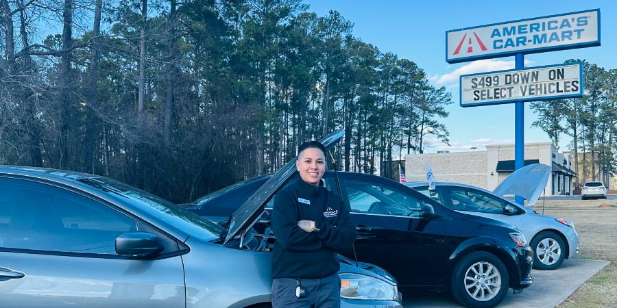 Car-Mart General Manager leaning against the side of a car in a row of vehicles at a Car-Mart dealership