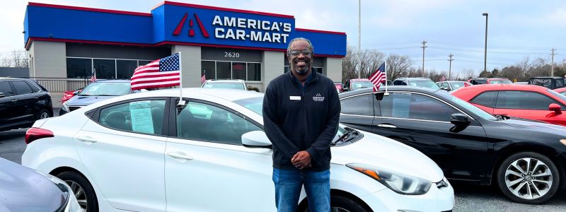 Car-Mart of Rogers North General Manager, Nakia Wimberley, leaning against the side of a white sedan in a row of vehicles at a Car-Mart dealership