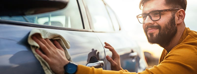 smiling man with glasses wiping the side of a car with a rag