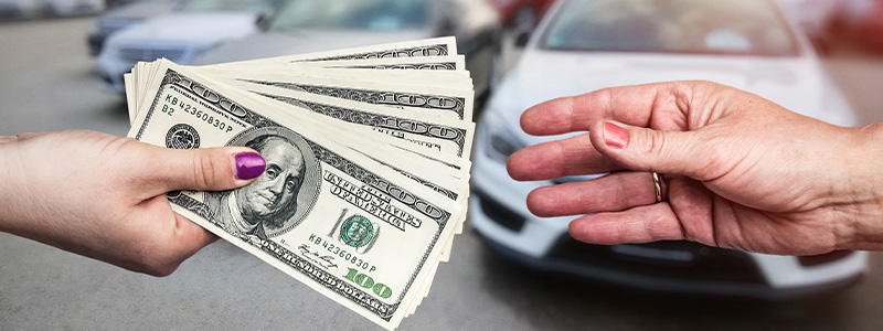 Total Cost of Car Ownership, one woman handing one hundred dollar bills to another woman with cars in the background