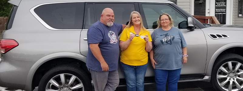 Customers Mike and Heidi Dudley with Car-Mart General Manager Pamela Turley stand by the Dudley's new car.