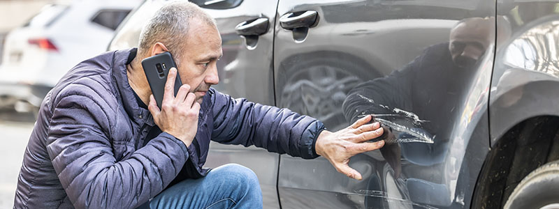 Man looking at scratch on his vehicle - on the phone